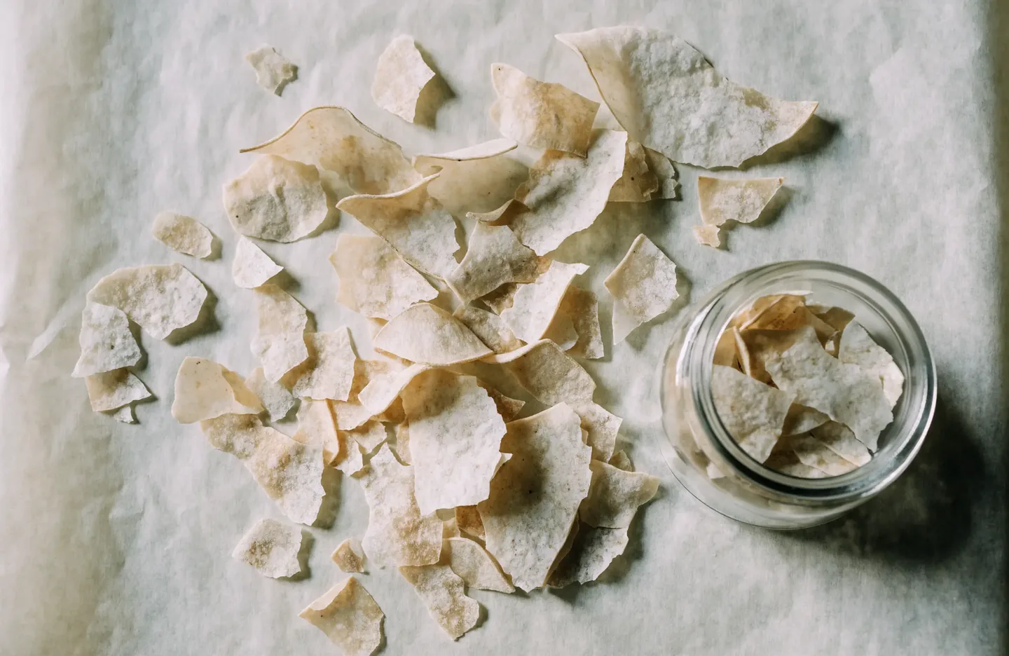 Thin brittle flakes of dried sourdough starter on baking parchment beside a small storage jar