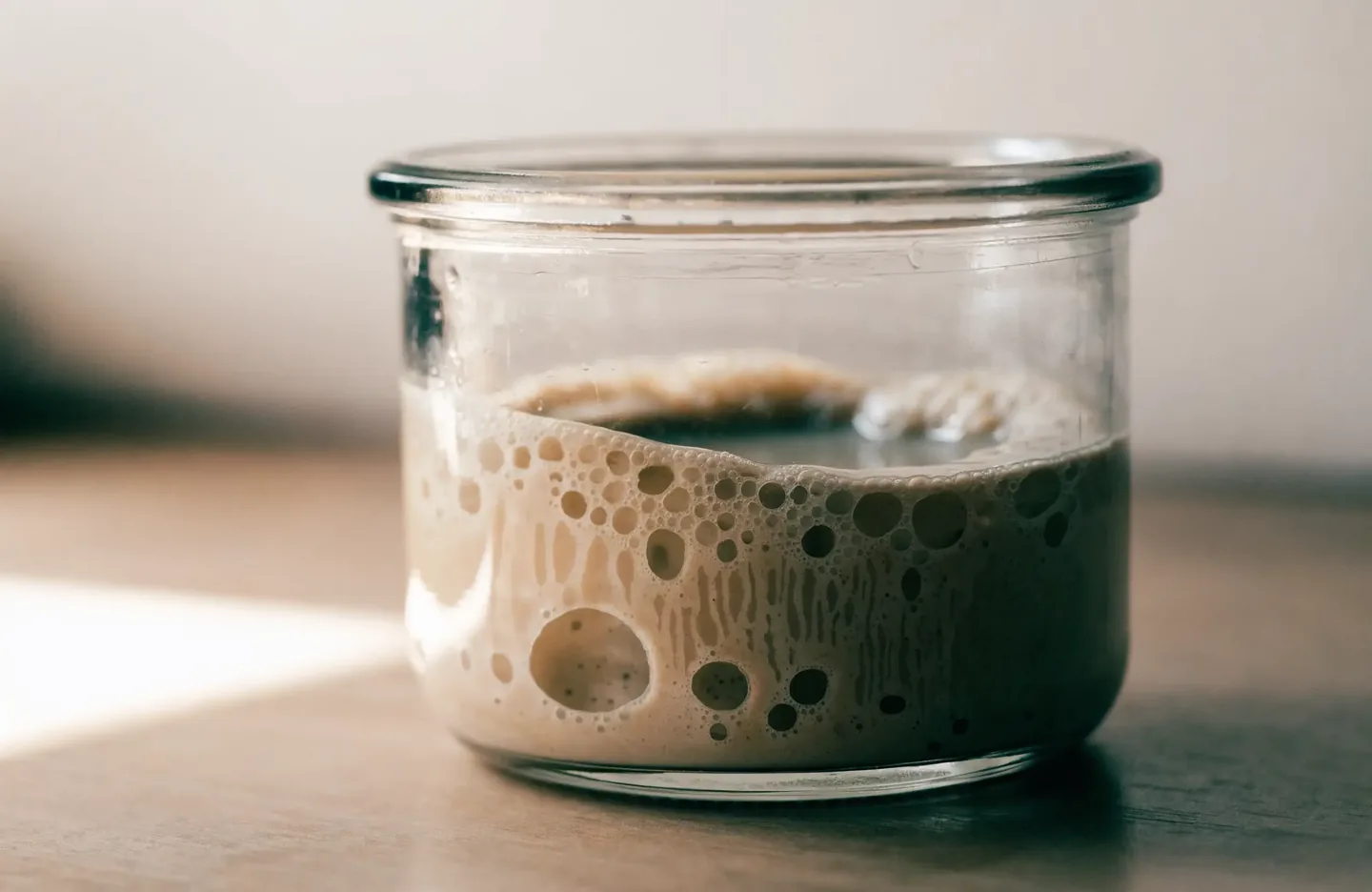 A jar of starter well past its peak: the surface has sunken in the centre and a layer of dark liquid has formed on top